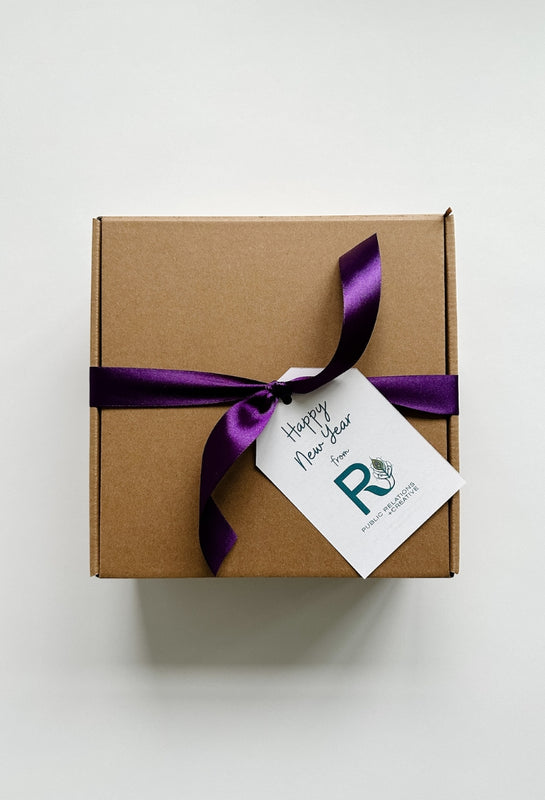A square Kraft gift box with purple ribbon and a Happy New Year tag. A perfect client appreciation gift for the new year.