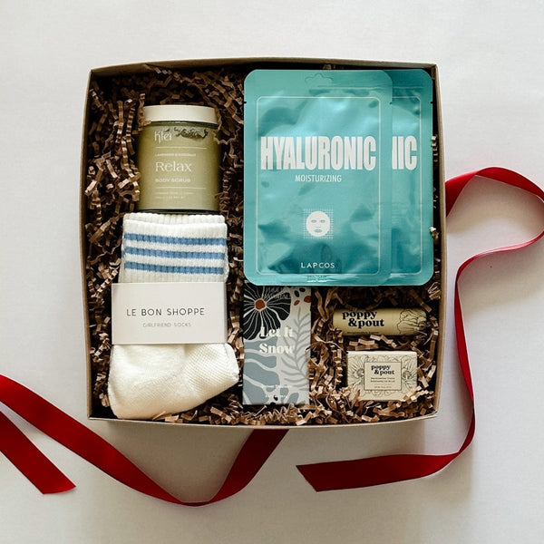 A relaxing spa gift set from East Third Collective that includes a LAPCOS face mask, cozy girlfriend socks, Klei body scrub, Thulisa shower steamers, and poppy and pout mint lip scrub and balm.