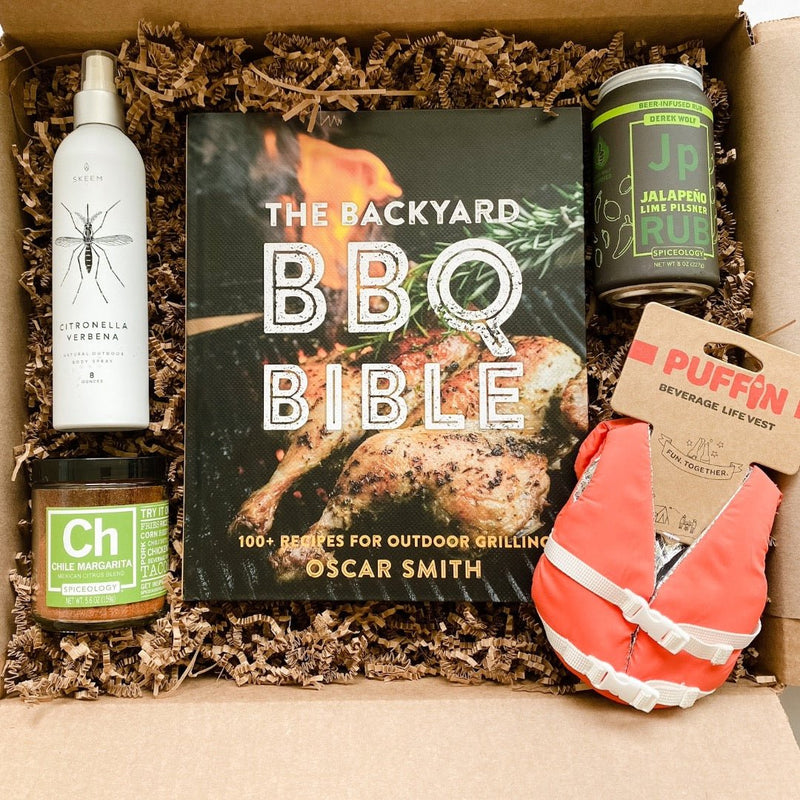A gift box for him including citronella bug spray, Chile margarita spice form Spiceology, the Backyard BBQ Bible cookbook, Spiceology Jalapeño Lime Pilsner rub, and a Puffin orange life vest beverage koozi.