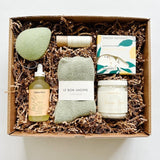 The ultimate spa gift featuring a green konjac sponge, cozy socks, body oil, body butter and lip balm from Butter Love Skin, and shower steamers from Thulisa Naturals.