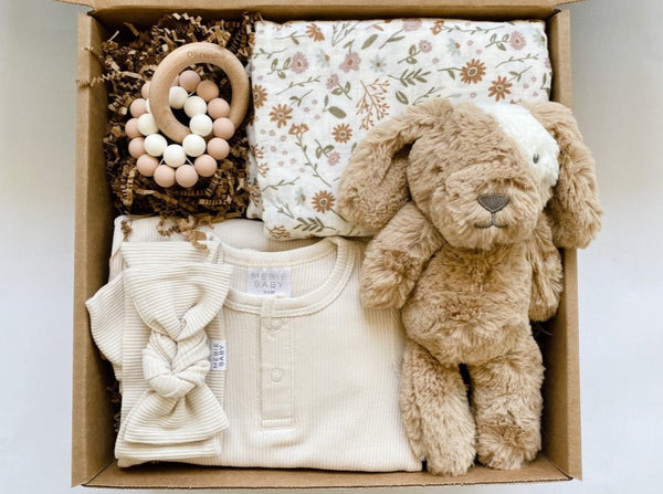 Mebie baby gown and bow paired with muslin swaddle blanket, stuffed pup, and a teether for a nuetral but adorable baby gift.
