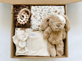 Mebie baby gown and bow paired with muslin swaddle blanket, stuffed pup, and a teether for a nuetral but adorable baby gift.