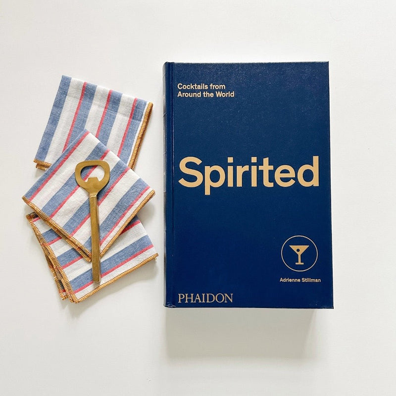 Mondrian striped cocktail napkins from Willow Ship, a gold bottle opener and a blue cocktail book titled Spirited.
