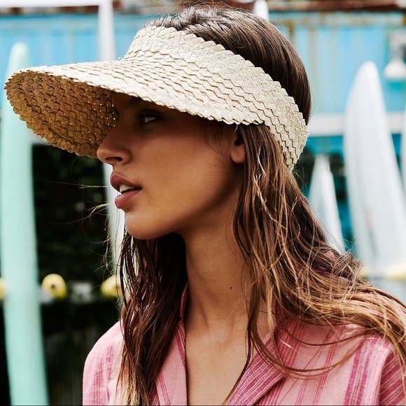 A brown haired woman in a pink shirt wearing a Straw Sun Visor from Bali Harvest.