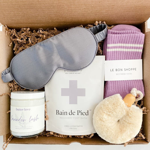 A relaxing gift for her that includes Butterlove lavender lush, a soft sleep mask, pursoma recovery foot bath, cozy boyfriend socks from le bon shoppe and a dry brush.