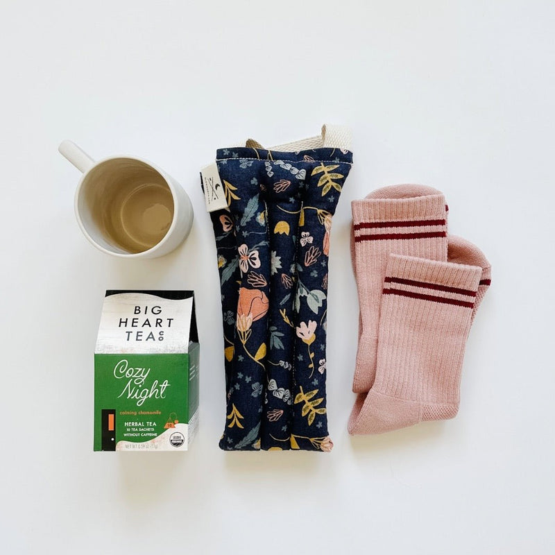 A sweet self-care gift for her with the slow north neck therapy wrap, big heart tea cozy night tea, le bon shoppe girlfriend socks, and a white mug.