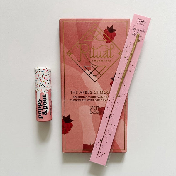 A small confetti lip balm from Poppy and Pout, a pink wrapped Aprés Chocolate bar from Ritual Chocolate, and a fun birthday wish sparkler on top of the chocolate bar.
