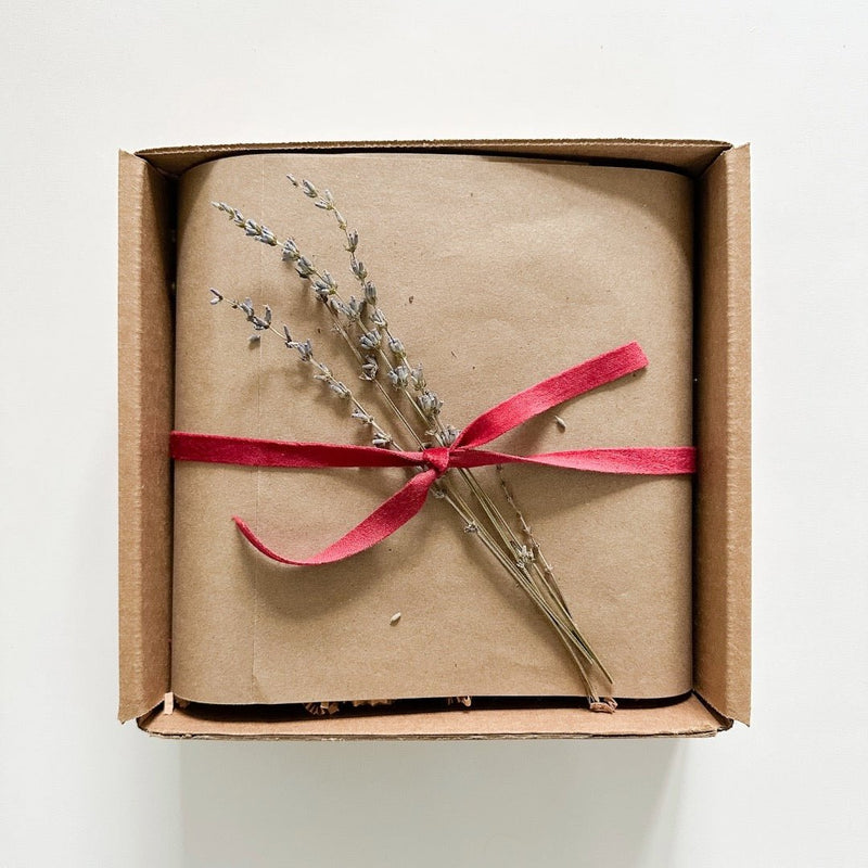 A Kraft gift box with Kraft paper and a few sprigs of lavender ties with a red ribbon.